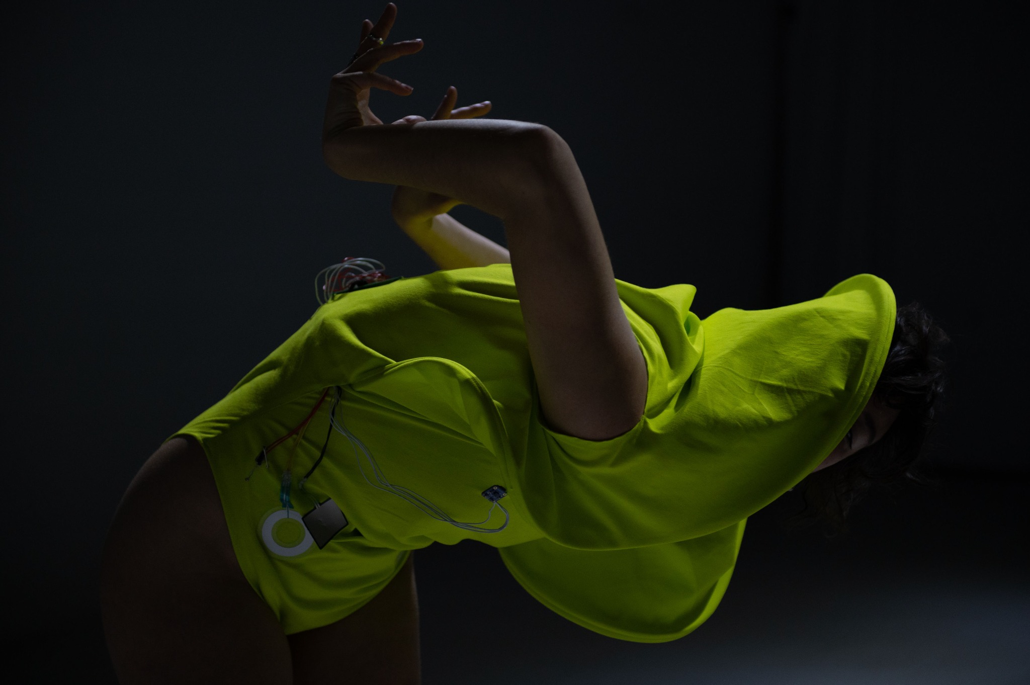 Performer bending backward in a yellow sonic garment with visible electronic components