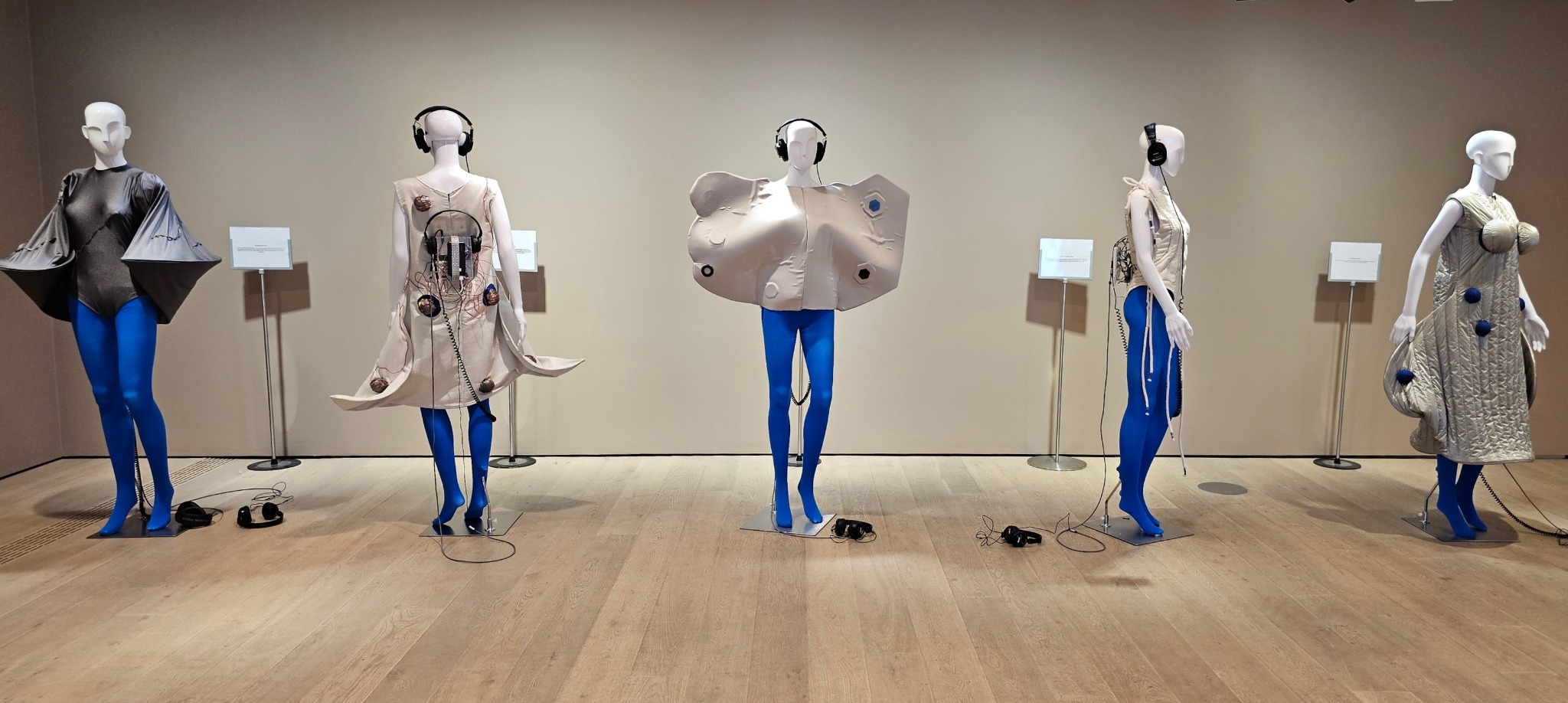 Five Pillow Talk sound sculptures displayed on mannequins with blue legs and headphones in a gallery